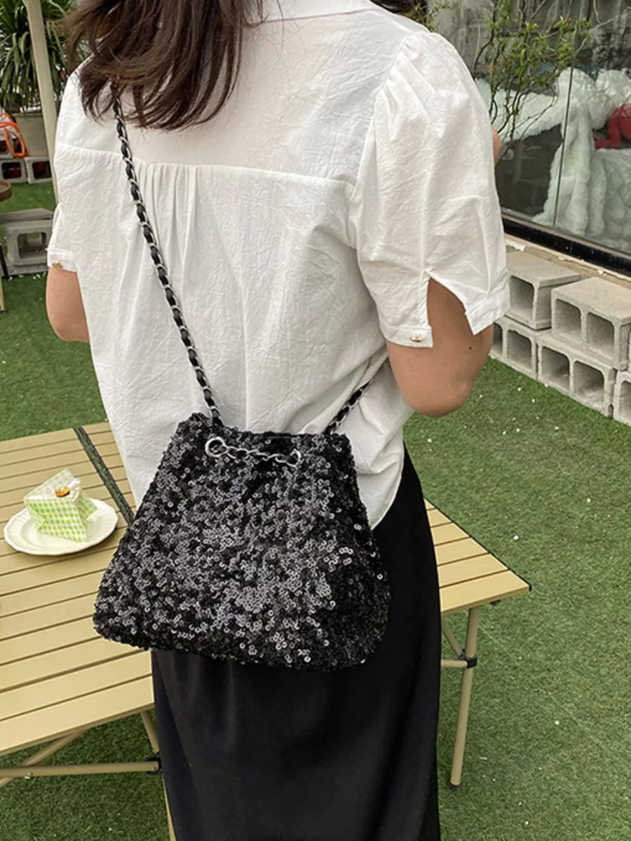 Black sequin bucket bag with chain strap and drawstring closure.