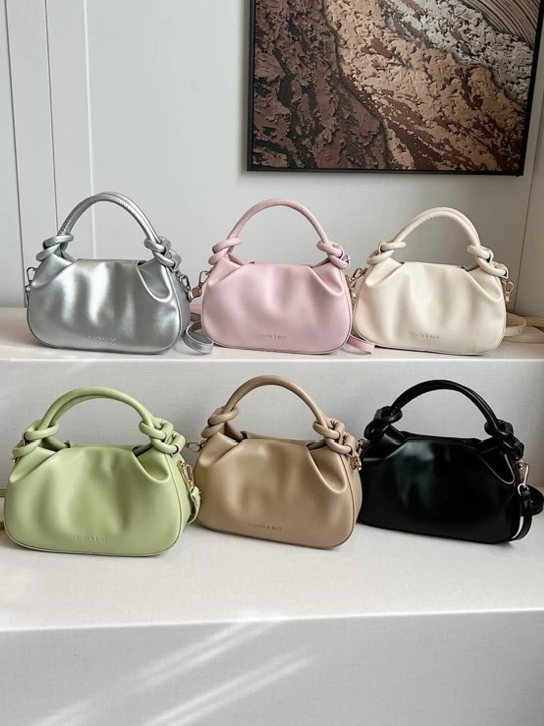 Mini ruched crossbody bags in black, pink, green, gray, silver, and cream with knotted handles.