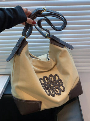 Khaki canvas tote bag with brown leather trim and embroidered logo detail