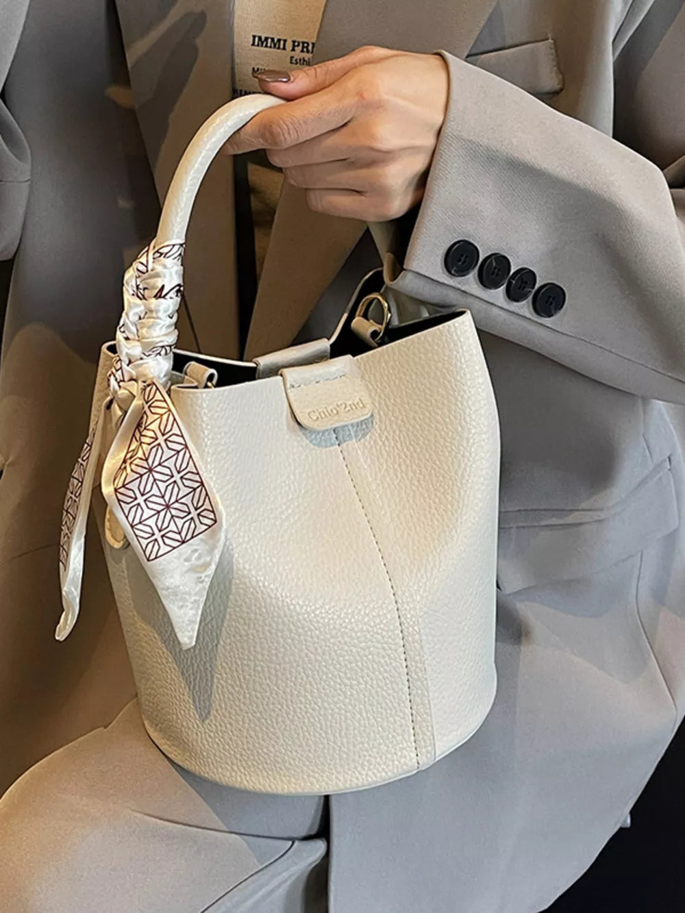 Beige pebbled leather bucket bag with patterned scarf tied to handle