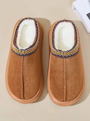 Caramel shearling house slippers with embroidered trim and plush lining.