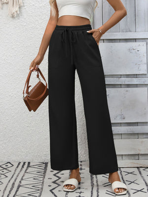 Black relaxed drawstring wide-leg pants with pockets, styled with a white crop top and brown bag.
