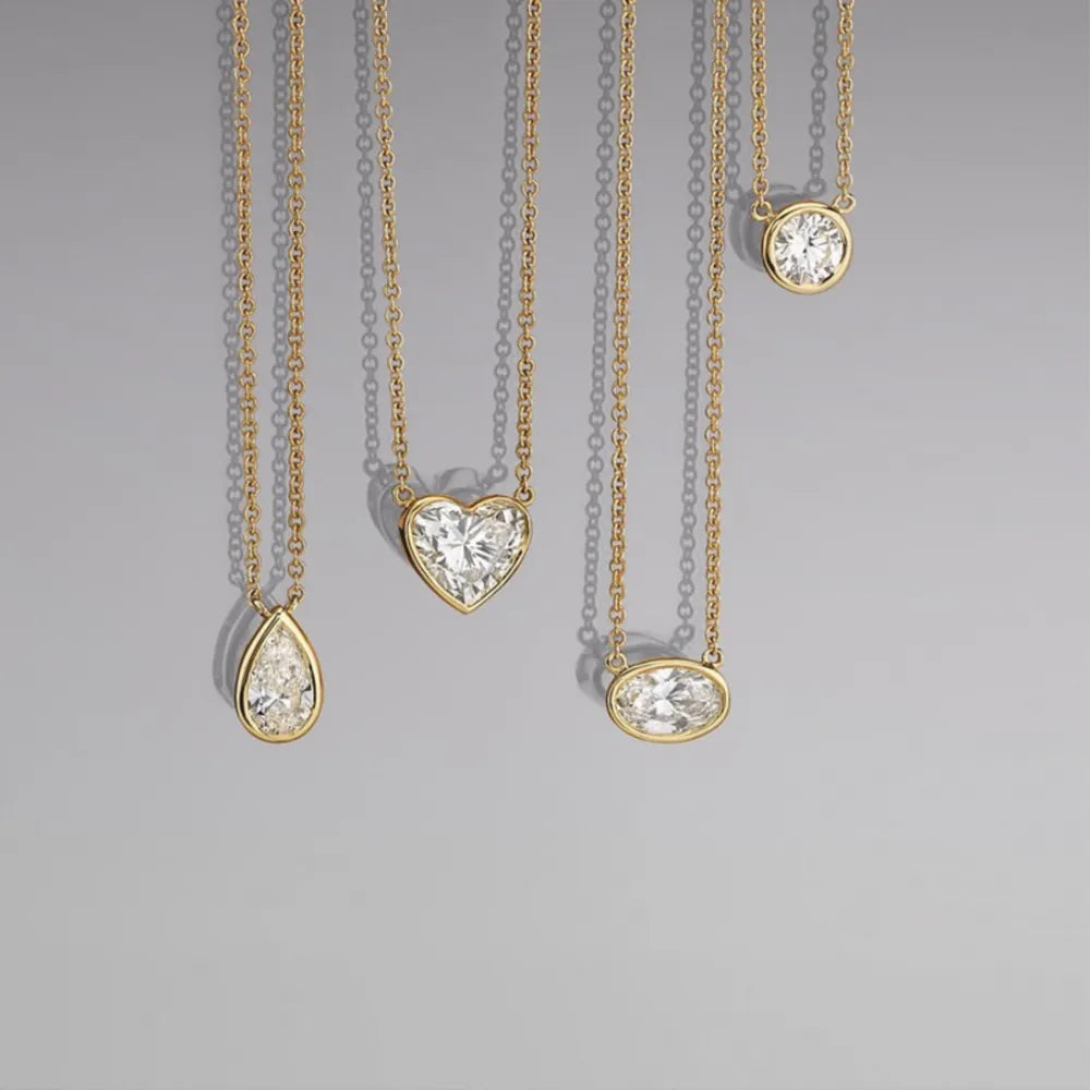 Bezel-set diamond solitaire necklaces in 18K gold-plated metal, featuring pear, heart, oval, and round cuts.