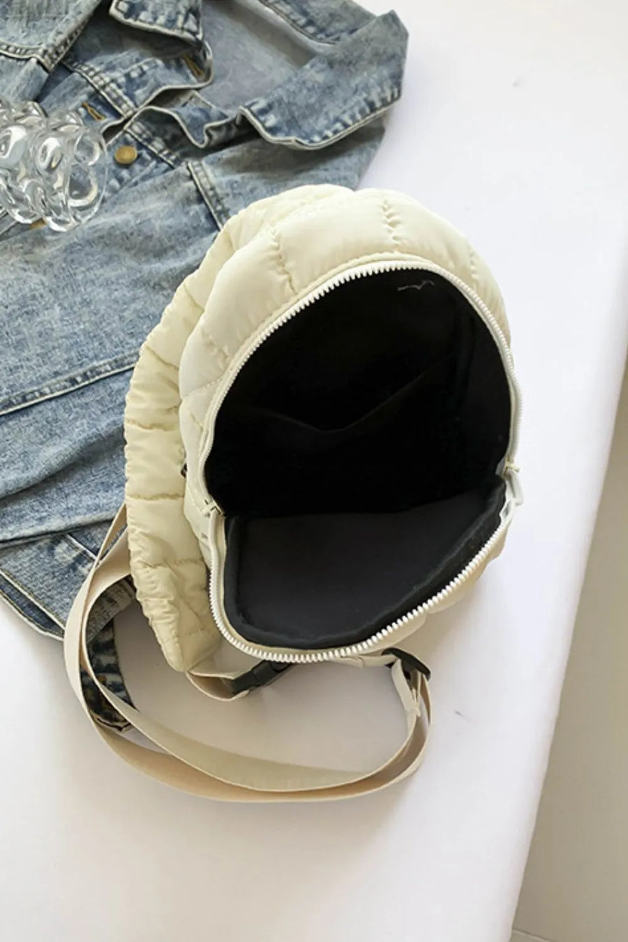 Padded sling bag in ivory with quilted detail and top handle, open to show interior.