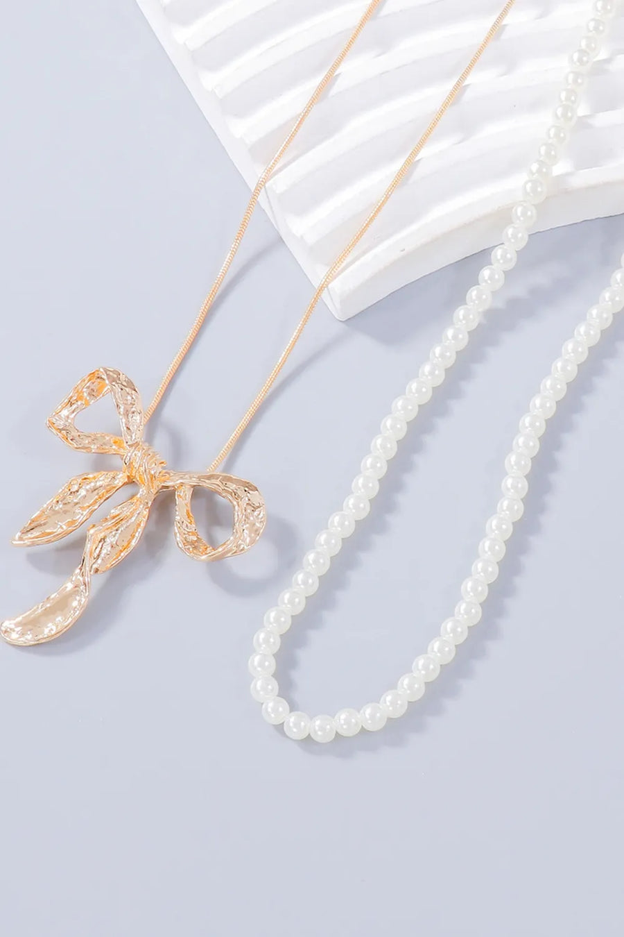 Textured bow pendant necklace and pearl necklace set in gold and white.