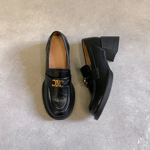 Black patent leather loafers with chunky sole and gold buckle detail.