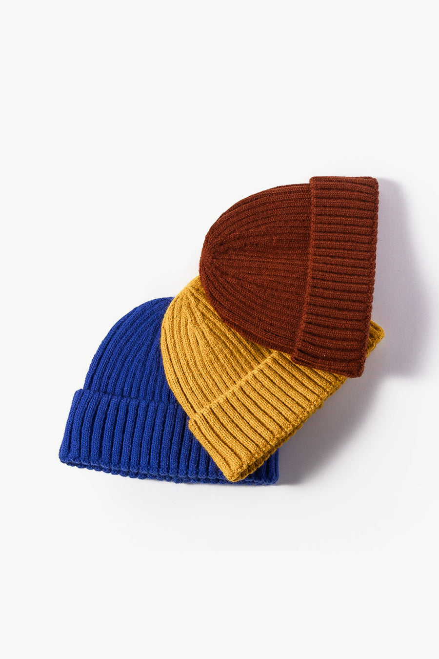 Chunky ribbed knit beanies in blue, mustard, and brown with folded cuffs.