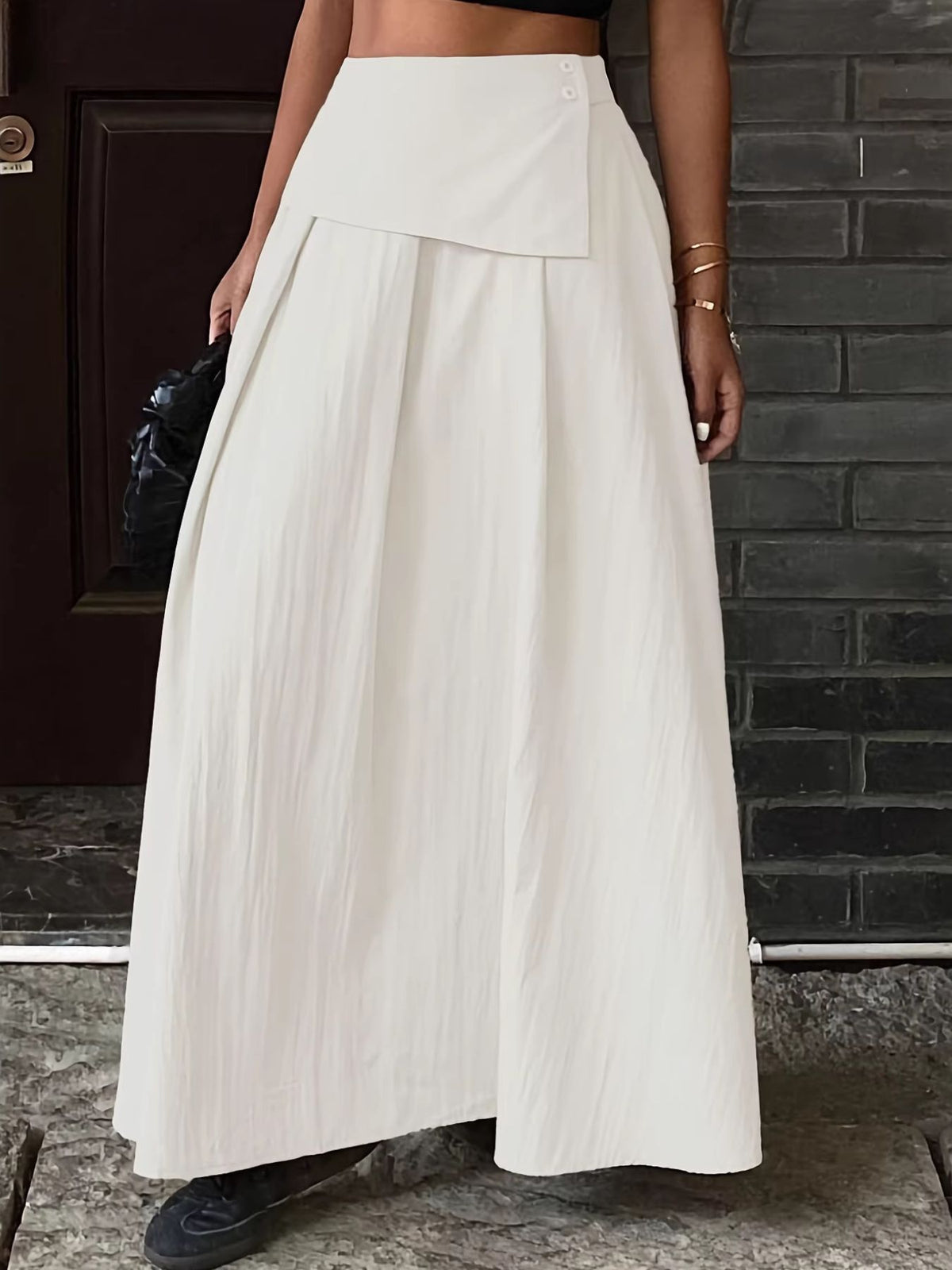 Pleated high-waisted maxi skirt in cream with button detail and a wrap-style overlay.