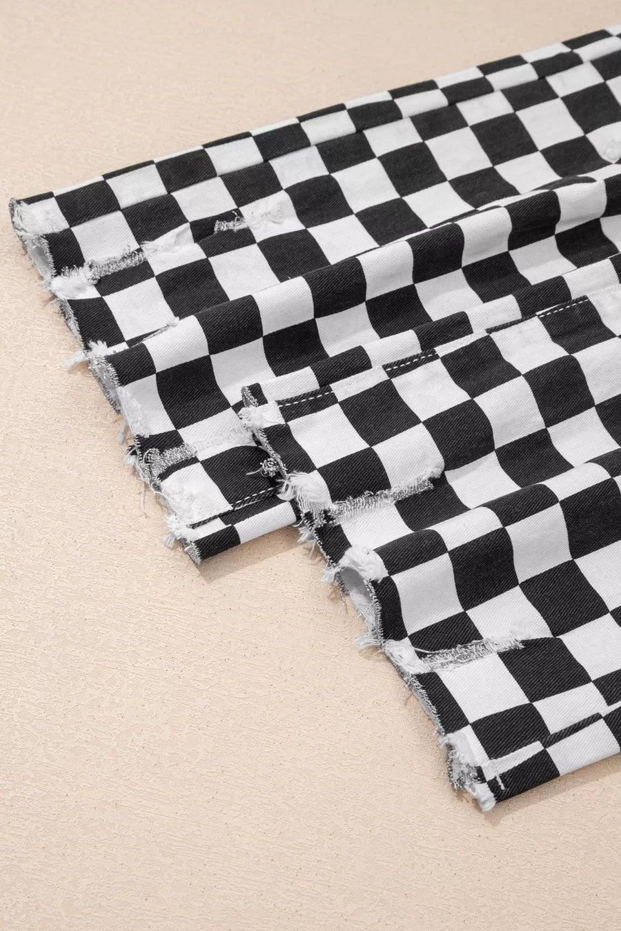 Checkerboard distressed cropped jeans in black and white denim with raw hem detail.