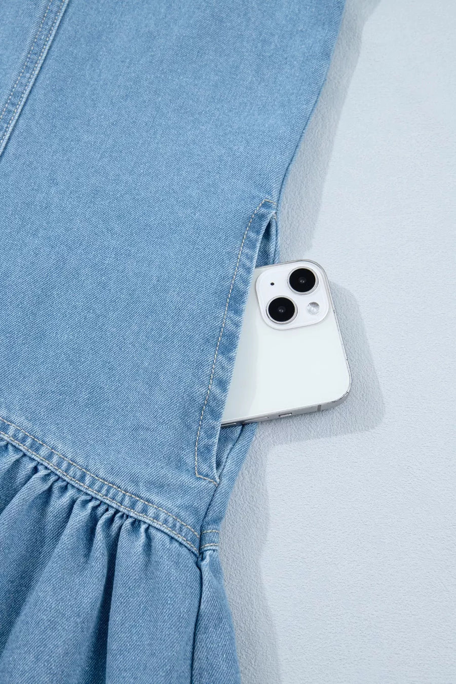 Light wash denim dress with ruffled hem and side pocket holding a phone.