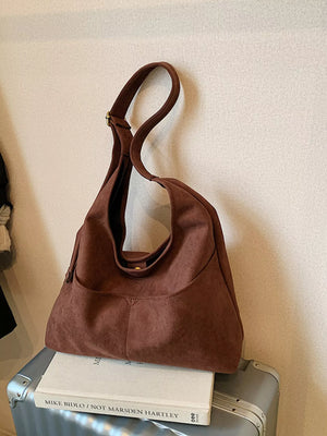 Brown suede shoulder bag with adjustable strap and front pocket detail.