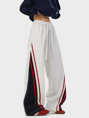 Men's gray drawstring casual pants with red and navy side stripe details.