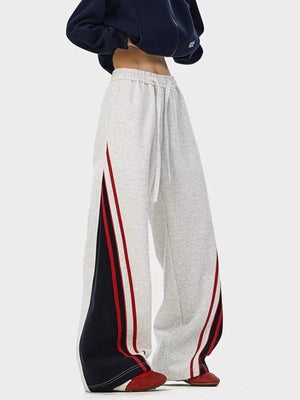 Men's gray drawstring casual pants with red and navy side stripe details.