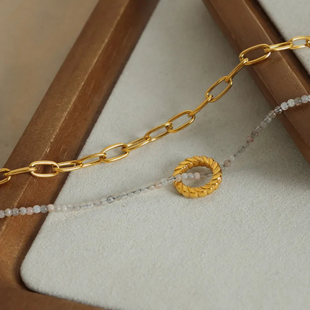 Gold layered chain necklace with beaded strand and twisted ring pendant.