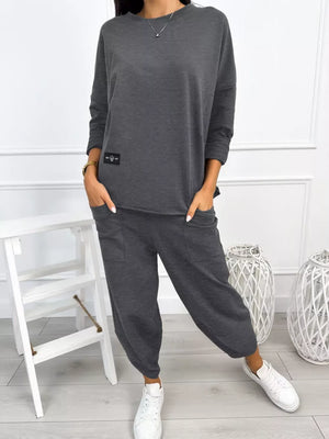 Dark gray two-piece lounge set with crew neck top and cuffed pants, featuring pockets.