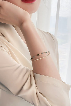 Dual chain bracelet with green stones and gold bar detail on a woman's arm.