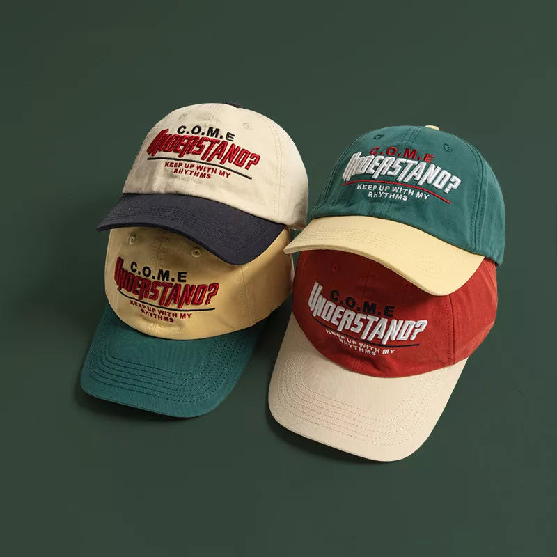 Embroidered baseball cap with "UNDERSTAND?" text detail, shown in cream, yellow, red, and green styles.