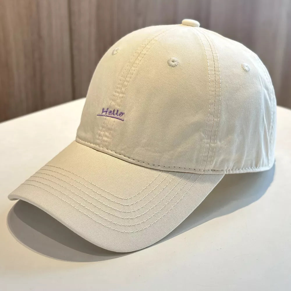 Beige baseball cap with purple embroidered "Hello" text detail.