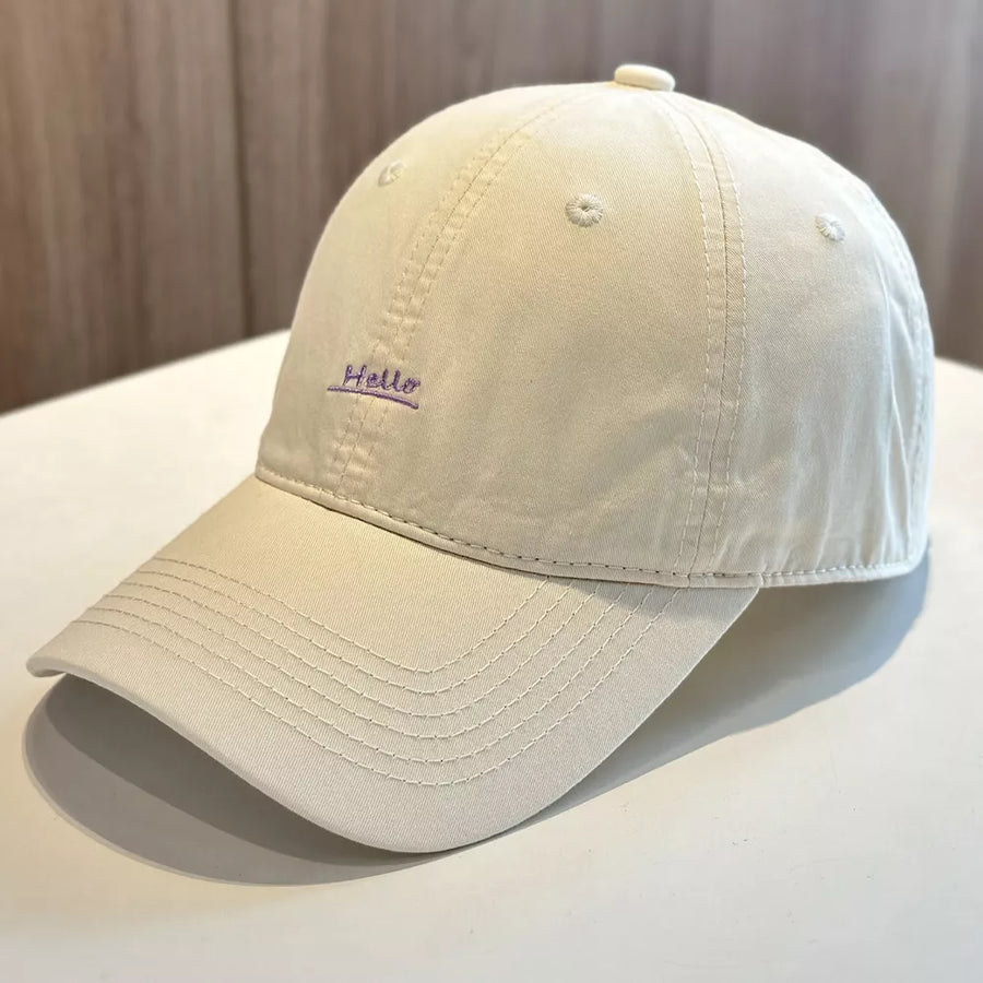 Beige baseball cap with purple embroidered "Hello" text detail.