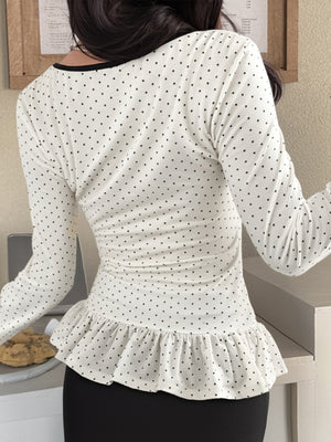 White polka dot long-sleeve t-shirt with ruffled hem and black trim neckline.