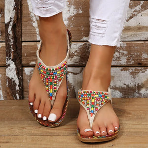 Beige thong sandals with colorful beaded embellishments and elastic ankle strap.