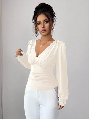 Beige ruched V-neck blouse with pearl embellishments and long sleeves.