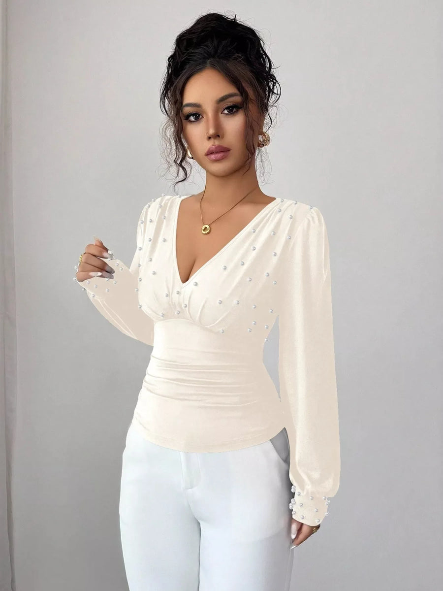 Beige ruched V-neck blouse with pearl embellishments and long sleeves.