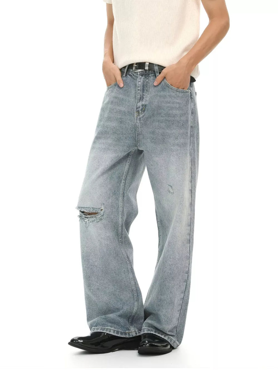 Light wash distressed denim jeans for men, wide-leg cut with a ripped knee detail.