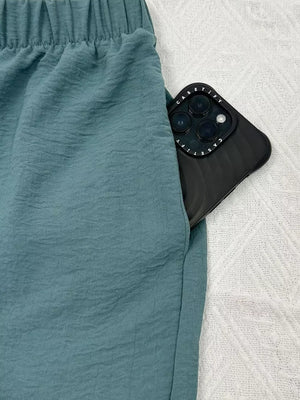 Turquoise wide-leg pants with elastic waist and side pocket holding a phone.