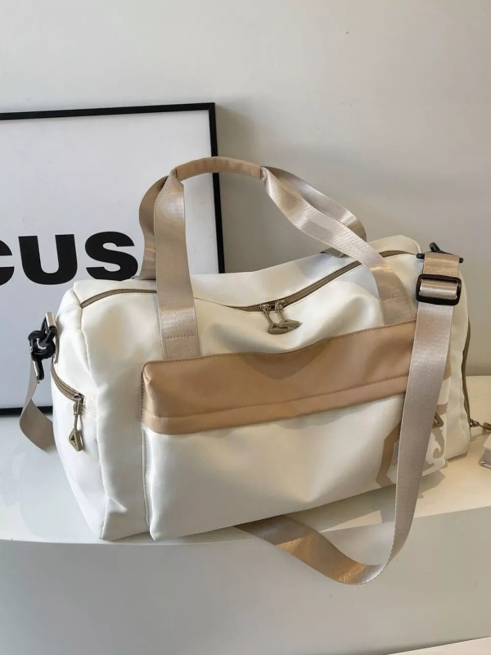Off-white Oxford cloth duffel bag with tan accents and detachable strap.