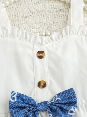 White cotton cami with sweetheart neckline, ruffles, buttons, and blue patterned bow.