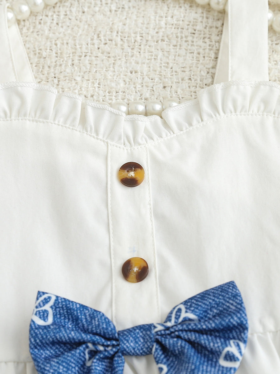White cotton cami with sweetheart neckline, ruffles, buttons, and blue patterned bow.