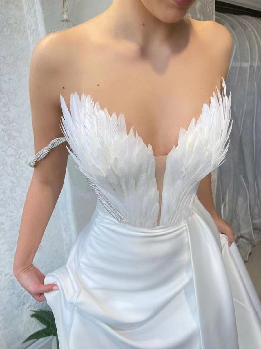 White feather embellished maxi dress with draped skirt and strapless neckline.