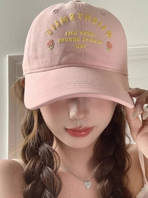 Pink baseball cap with yellow embroidered text and rose details.