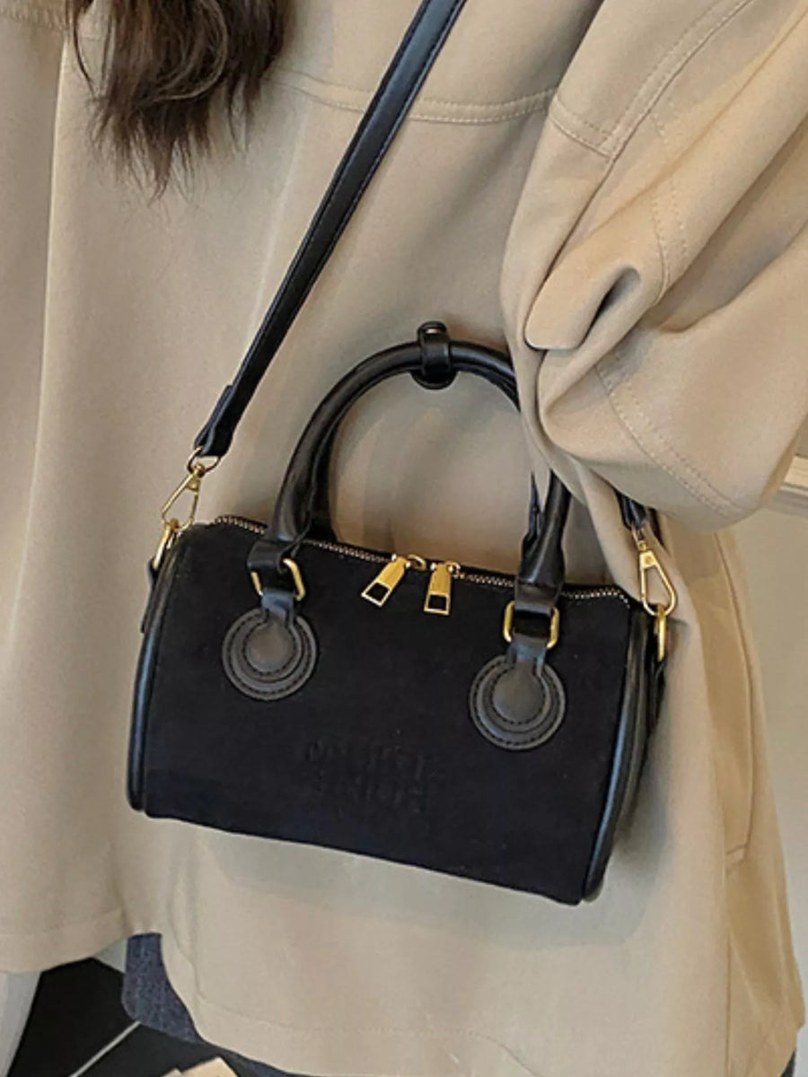 Black barrel crossbody bag with double top handles and gold hardware.