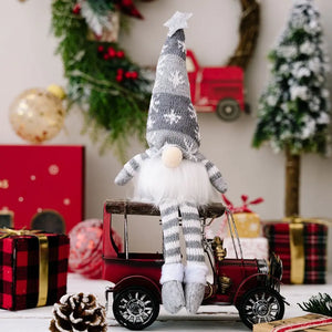 Illuminated knit gnome in gray with snowflake pattern, white beard, and striped legs sits on a red toy car.