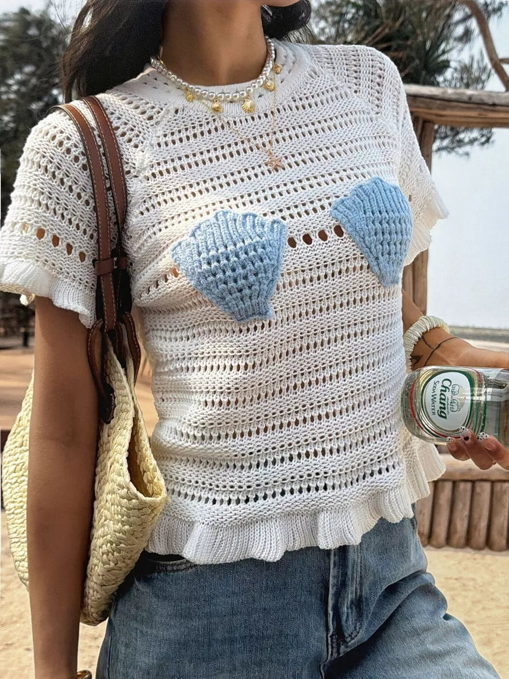 White crochet knit top with blue seashell appliqués and ruffled hem.