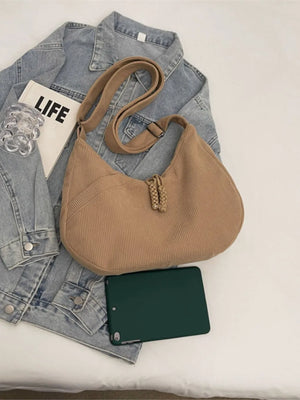 Beige corduroy crescent shoulder bag with braided detail and tassels.