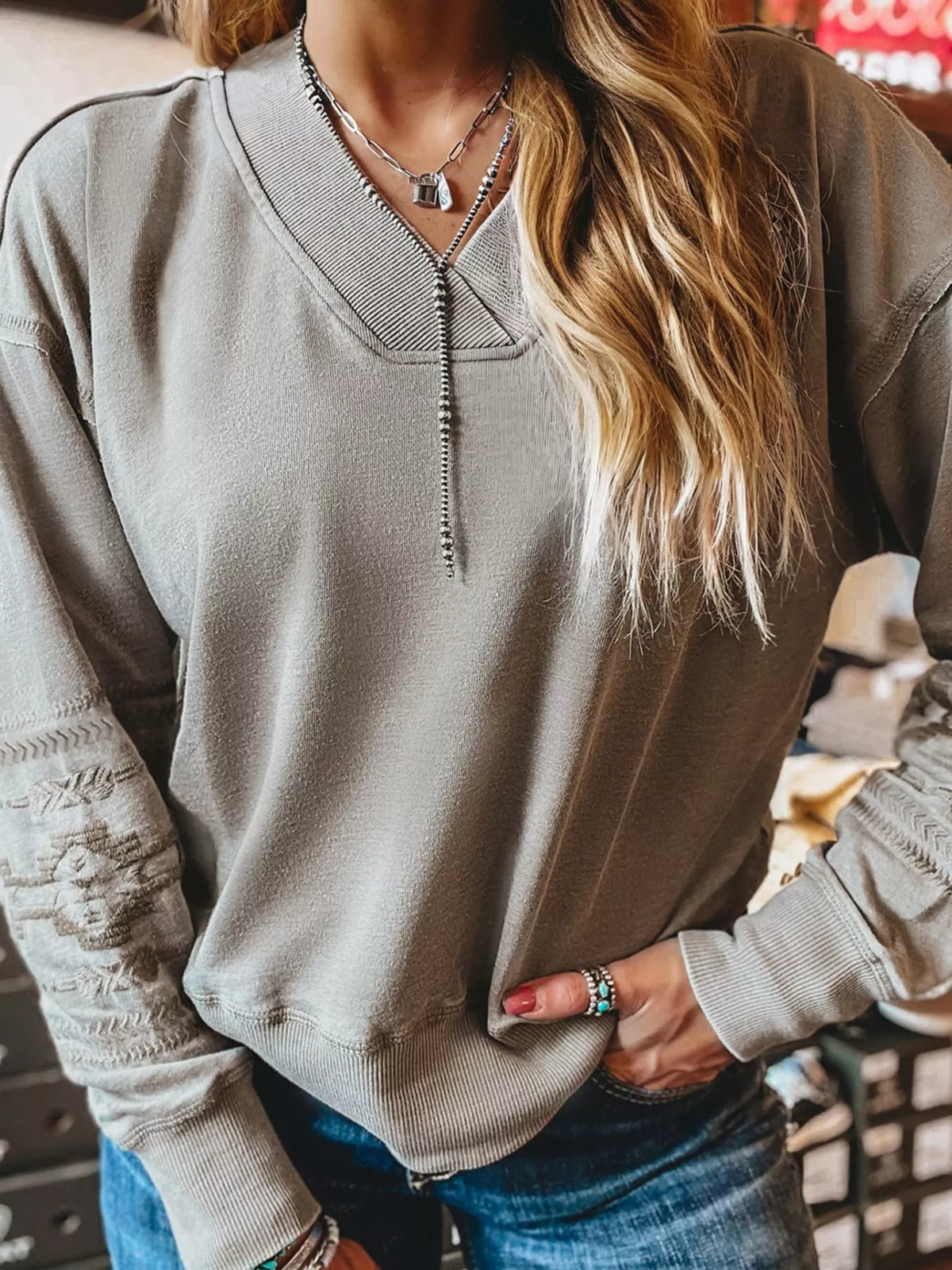 Gray V-neck sweatshirt with Aztec embroidery on sleeves and neckline detail.