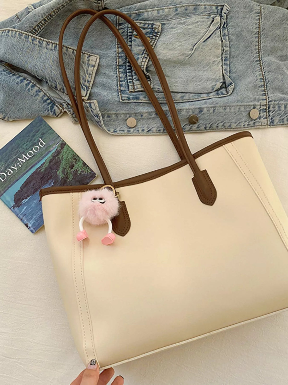 Sophisticated beige PU leather tote bag with brown trim and handles, featuring a fluffy pink charm.