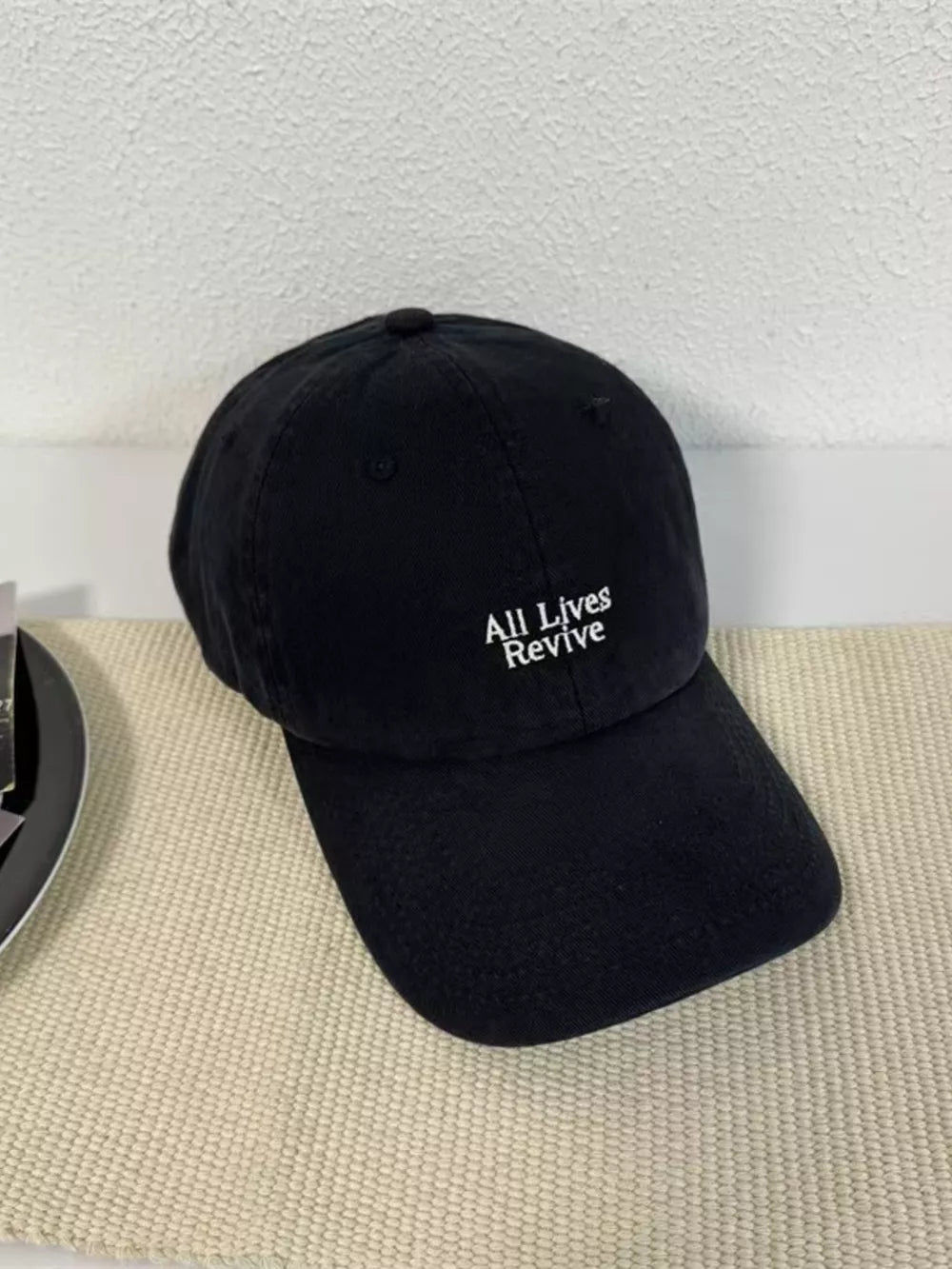 Black baseball cap with white embroidered "All Lives Revive" text.