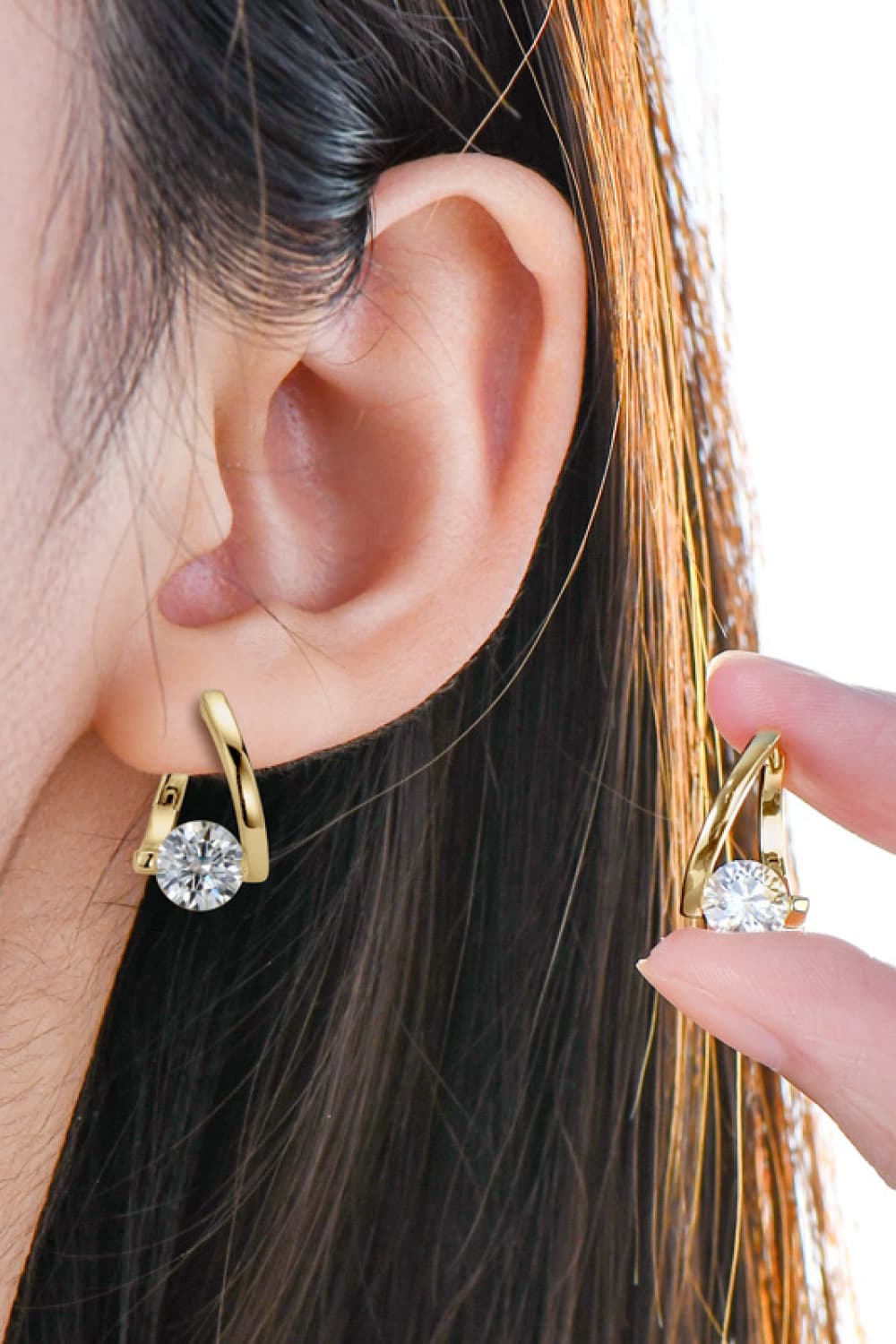Gold hoop earrings with a single diamond accent, worn by a woman.