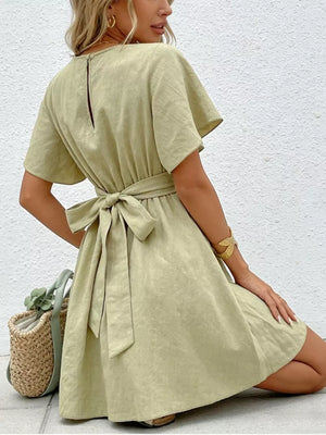 Light green mini dress with flutter sleeves, a tie waist, and buttoned back detail.