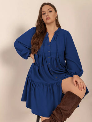 Plus-size dark blue A-line dress with tie-neck and button-front, tiered skirt.