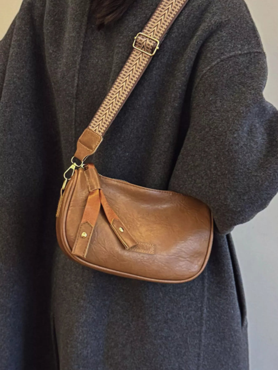 Brown leather crossbody bag with patterned strap and decorative tabs.