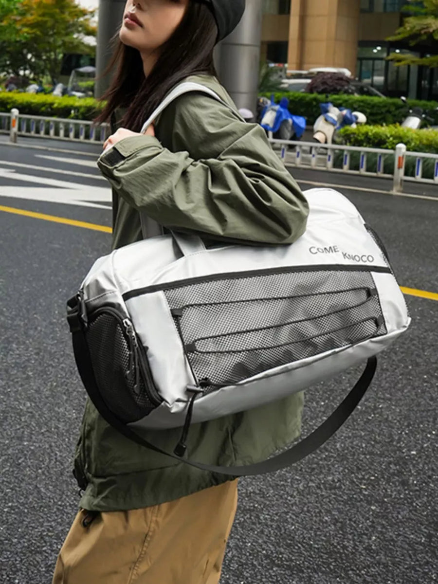 Sleek grey duffel bag with mesh pockets and adjustable strap, worn by a woman.