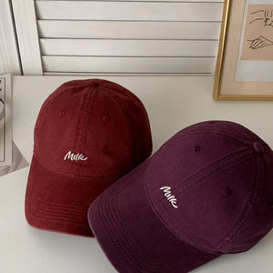 Embroidered letter baseball caps in wine red and purple with white "Milk" text.