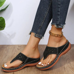 Black laser-cut thong sandals with white stitching and architectural detail.