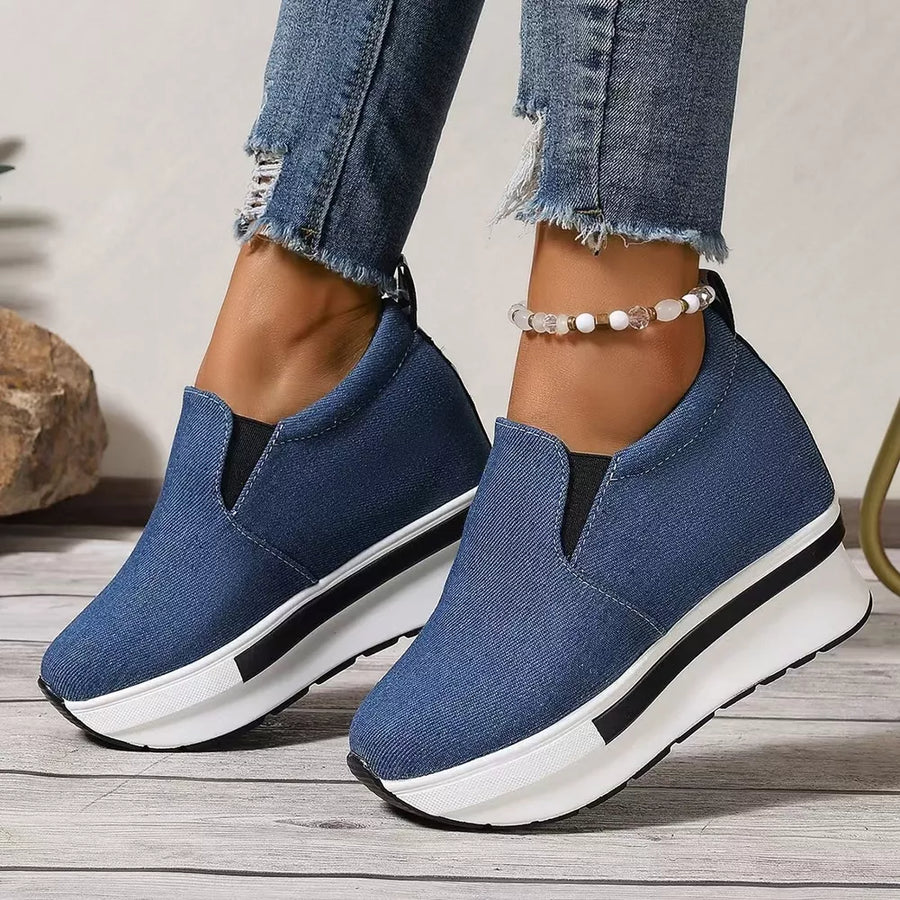 Blue denim slip-on platform shoes with a chunky white sole and black stripe detail.
