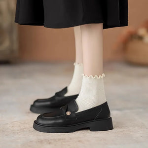 Black penny loafers with gold detail and platform sole, styled with ruffled socks.